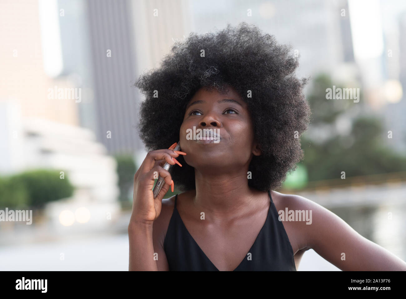 Une pensive African American Woman talking on a cell phone, gratte-ciel sur l'arrière-plan Banque D'Images