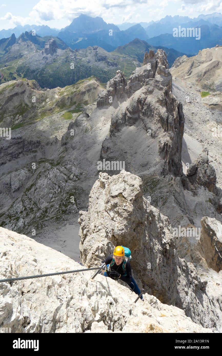 Vue verticale d'un grimpeur femelle sur une via ferrata dans les Dolomites italiennes avec une très belle vue derrière Banque D'Images