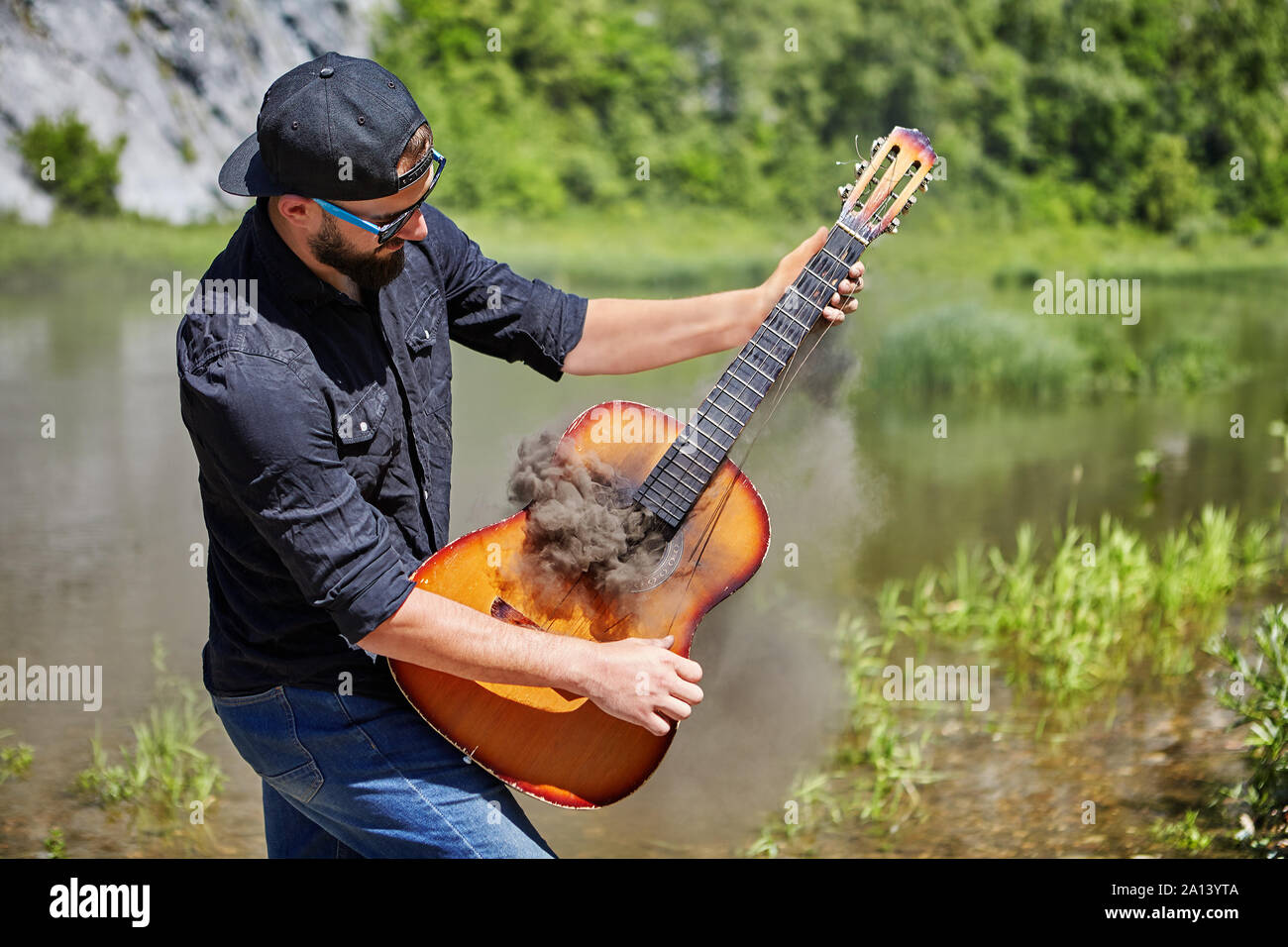 Un jeune homme, 23 ans, portant une casquette, lunettes de soleil, et une  chemise noire froissée, joue une guitare acoustique de l'épaisse fumée qui  vient. Le guitariste Photo Stock - Alamy