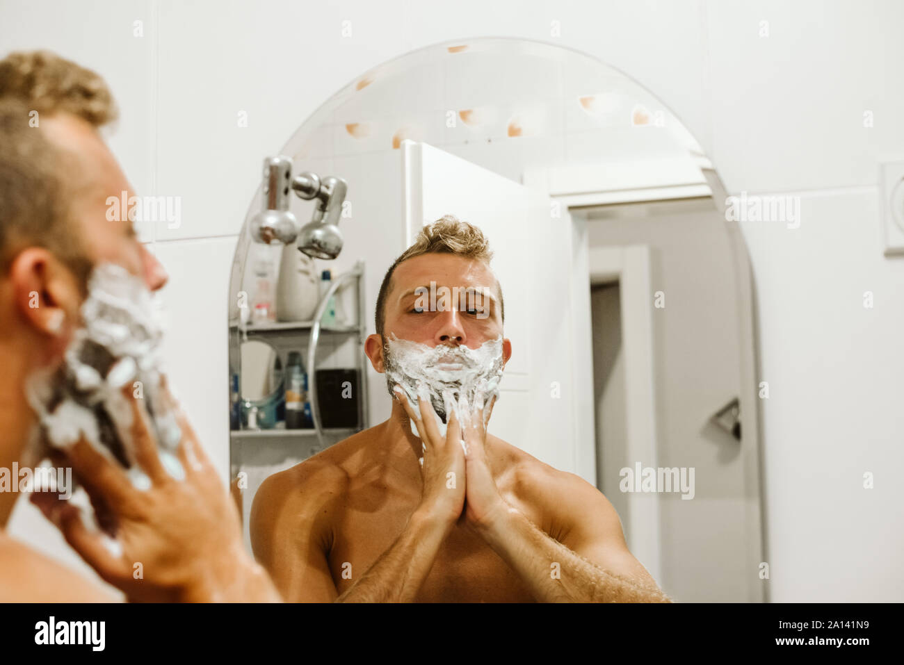 Man shaving face au miroir de salle de bains Banque D'Images