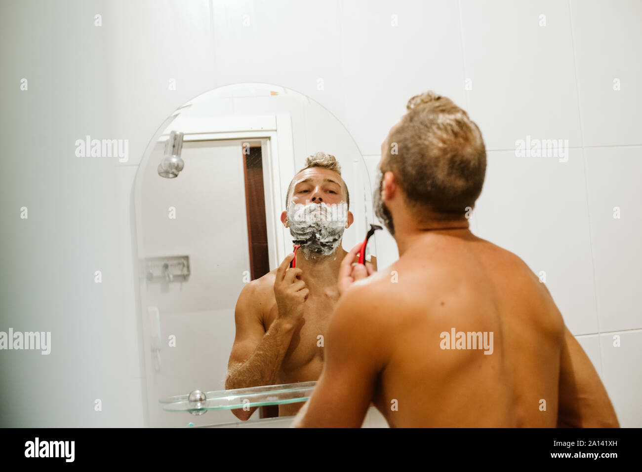 Man shaving face au miroir de salle de bains Banque D'Images