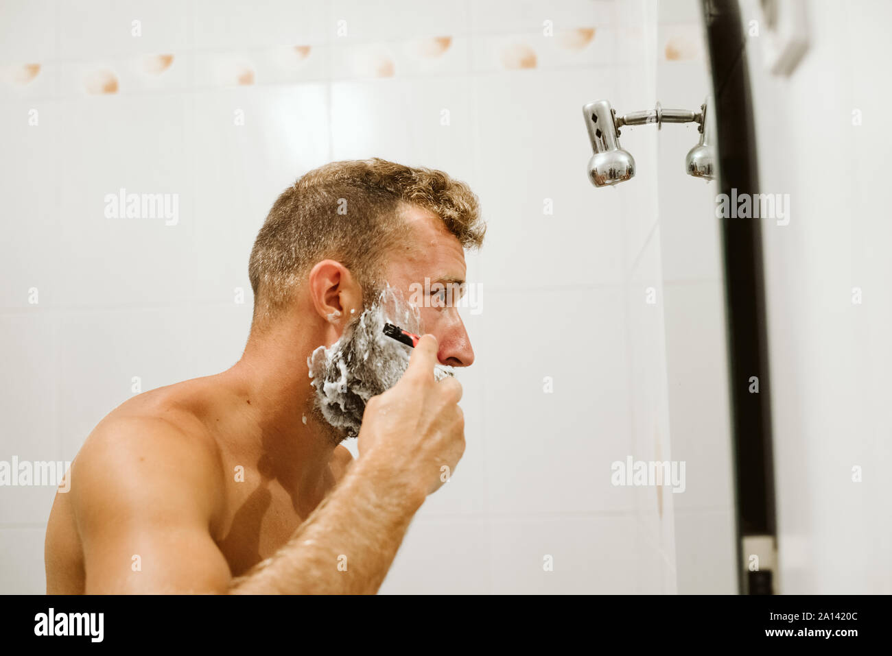 Man shaving face au miroir de salle de bains Banque D'Images