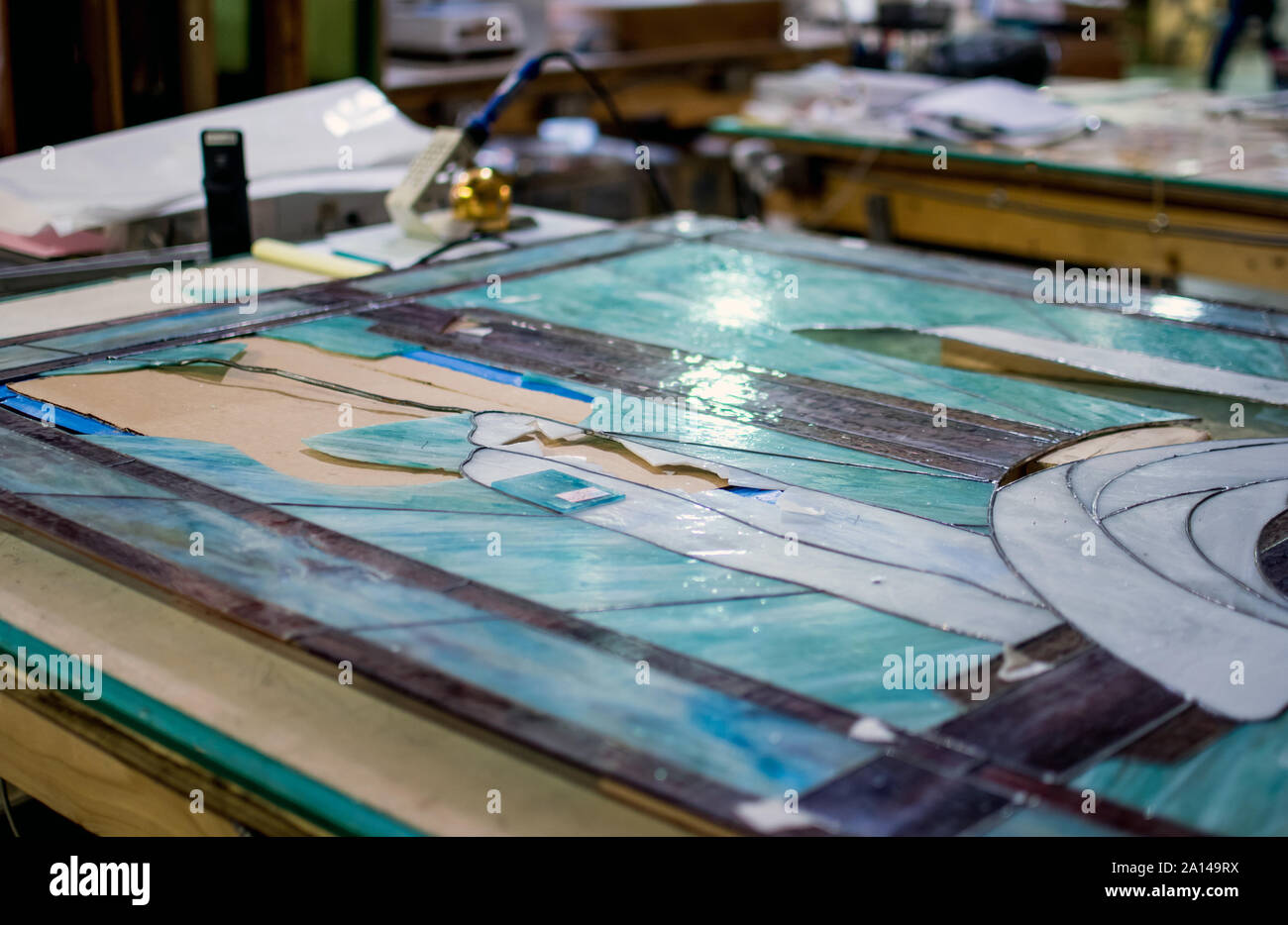 Un vieux vitrail repose sur une table de travail, avec des morceaux enlevés pour être réparés et remplacés Banque D'Images