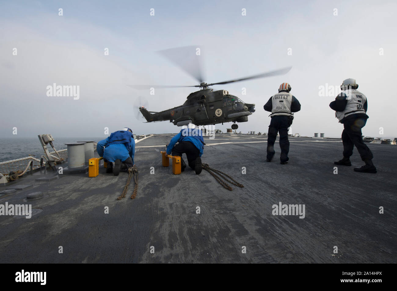 Les marins à bord de l'USS Ross se préparent à caler et la chaîne d'un hélicoptère Puma de la marine roumaine. Banque D'Images