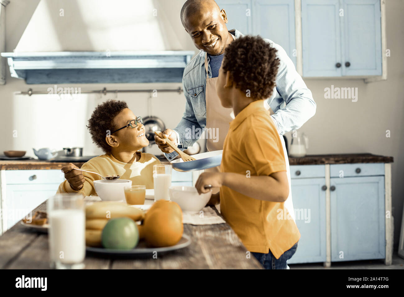 Dans la cuisine baignée de soleil un homme et ses deux fils de manger et discuter. Banque D'Images