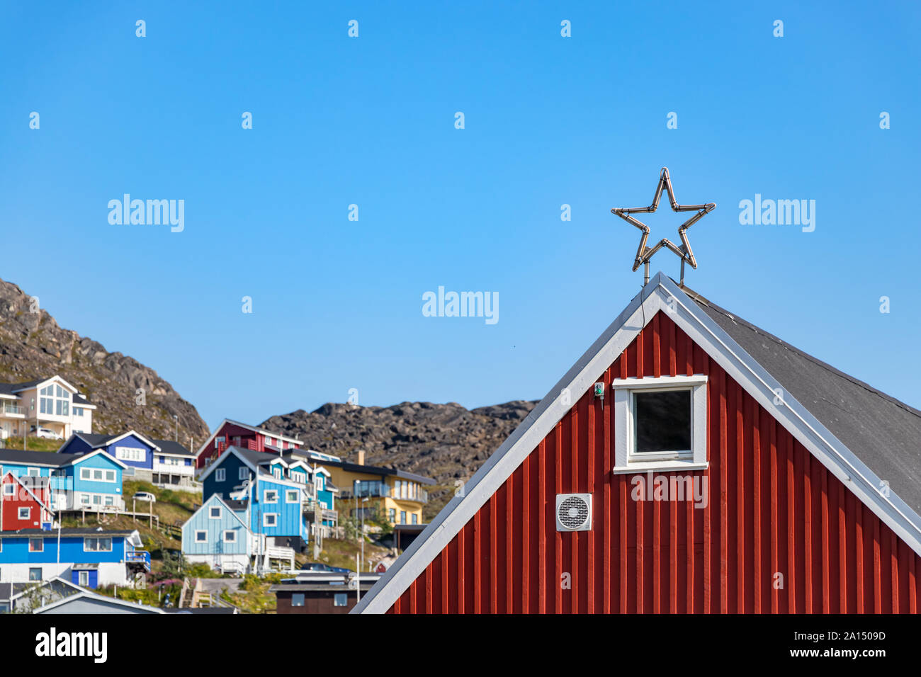 Une étoile sur le haut d'un toit de l'école locale et maisons colorées sur des collines rocheuses à Qaqortoq (Groenland). Banque D'Images