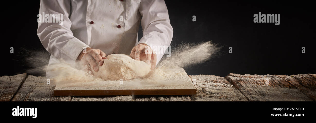 Motion gel explosion de farine cuisine comme un chef ou cuisinier travaille sur un monticule de pâte crue dans un tableau dans un cadre rustique avec bannière panorama savs copie Banque D'Images