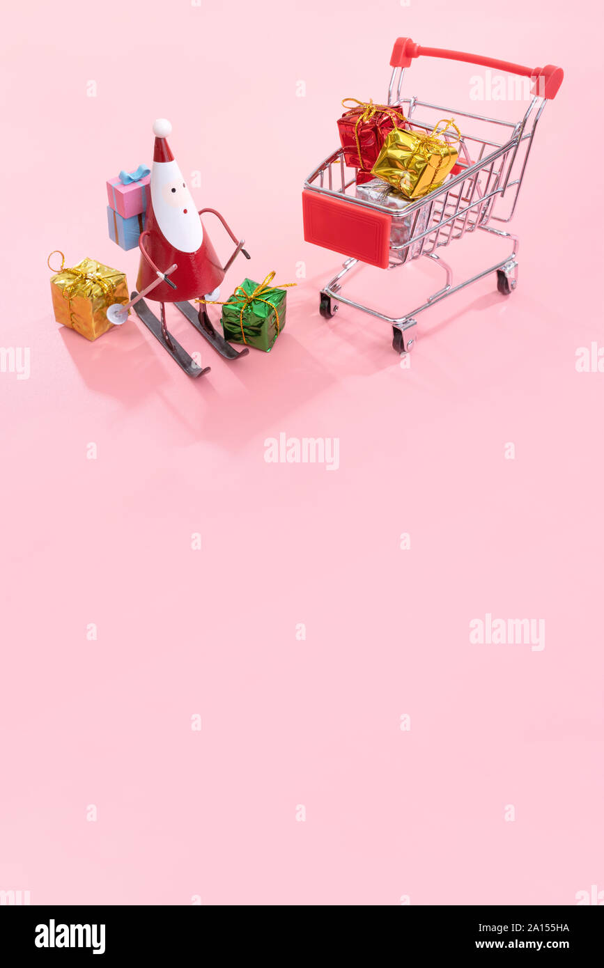 Concept d'achats de Noël, mini red shop panier trolley avec le Père Noël de jouets et de boîte-cadeau isolé sur fond rose pale, copie vierge de l'espace, Close up Banque D'Images