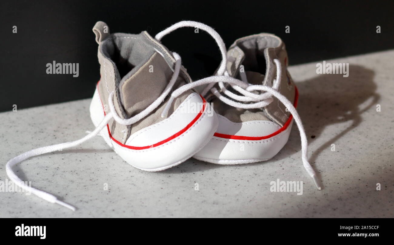 Unlaced minuscule bébé beige sneakers debout sur fond noir avec l'espace négatif. Concept de douche de bébé Banque D'Images