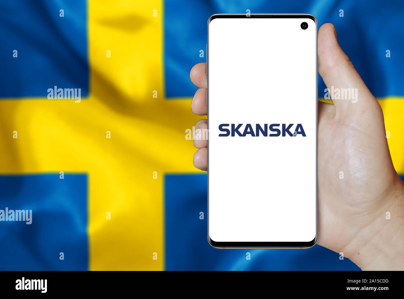 Un homme est titulaire d'un smartphone affichant le logo de la société Skanska énumérés sur OMX Stockholm. Drapeau suédois dans l'arrière-plan. Credit : PIXDUCE Banque D'Images