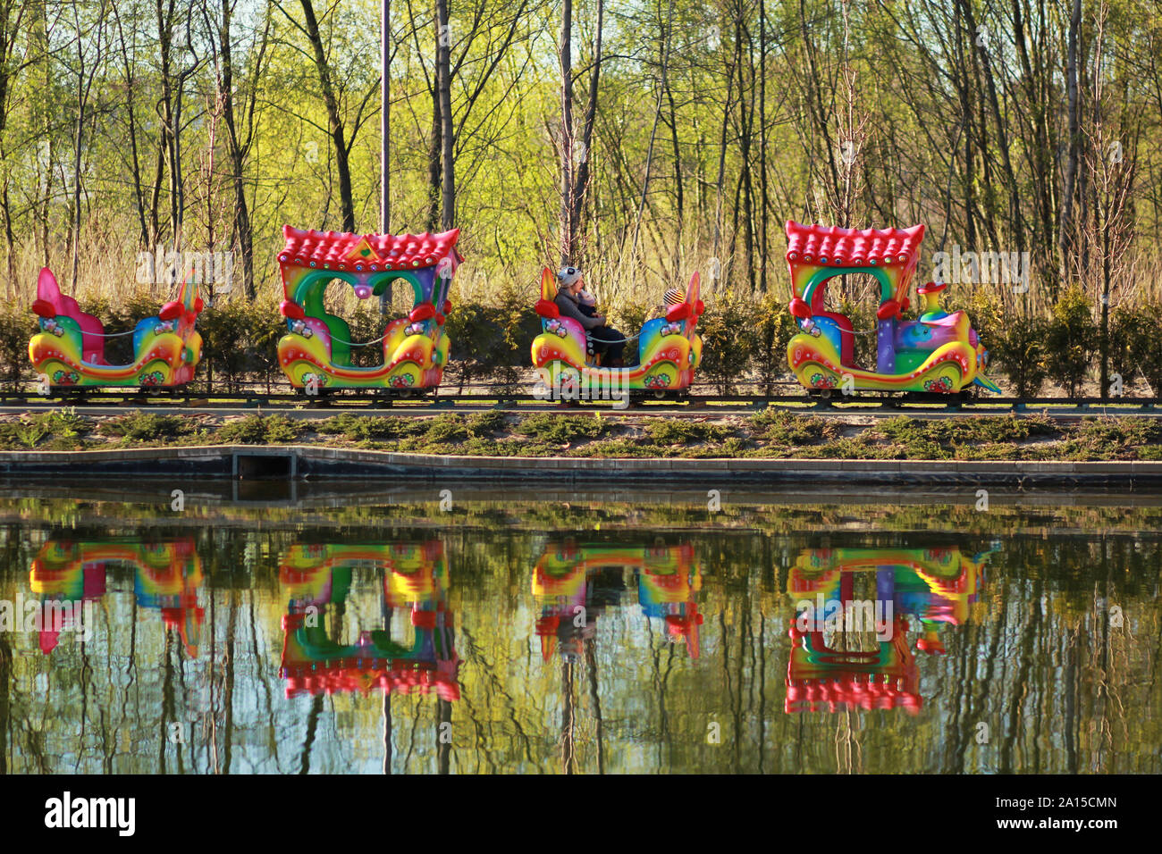 La mère et deux enfants équitation un carrousel coloré au printemps train parc, reflet dans un lac Banque D'Images