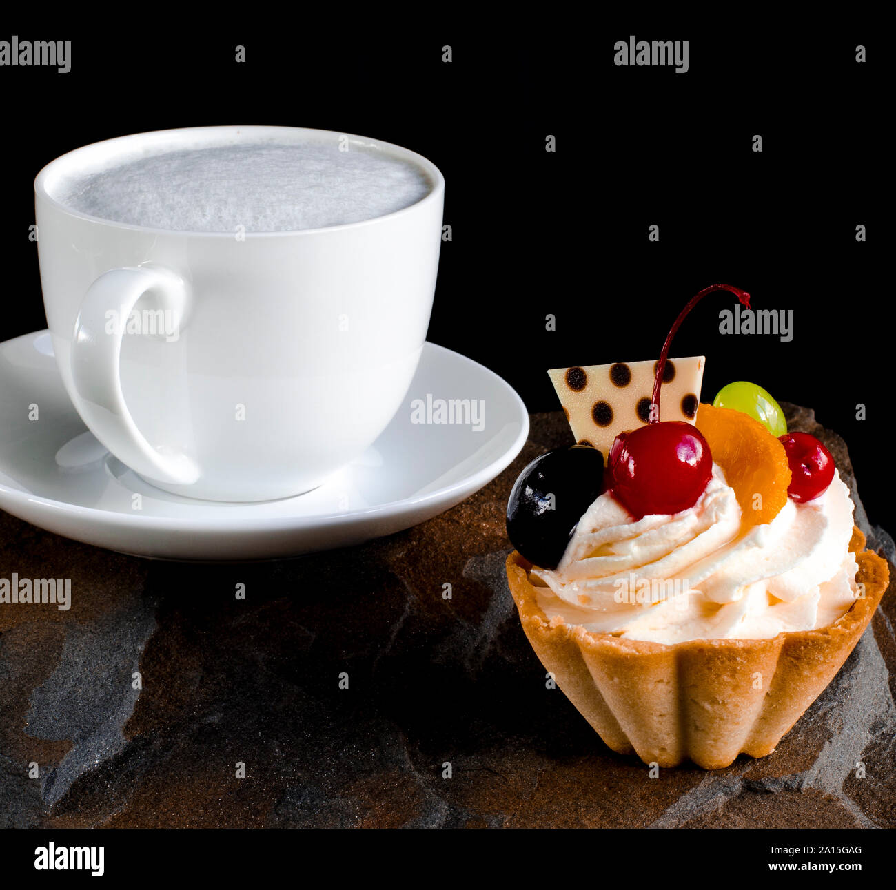 Un gâteau aux fruits avec les cerises, les raisins et les pruniers se dresse sur une pierre sauvage à côté d'une tasse de café blanc avec une mousse Banque D'Images