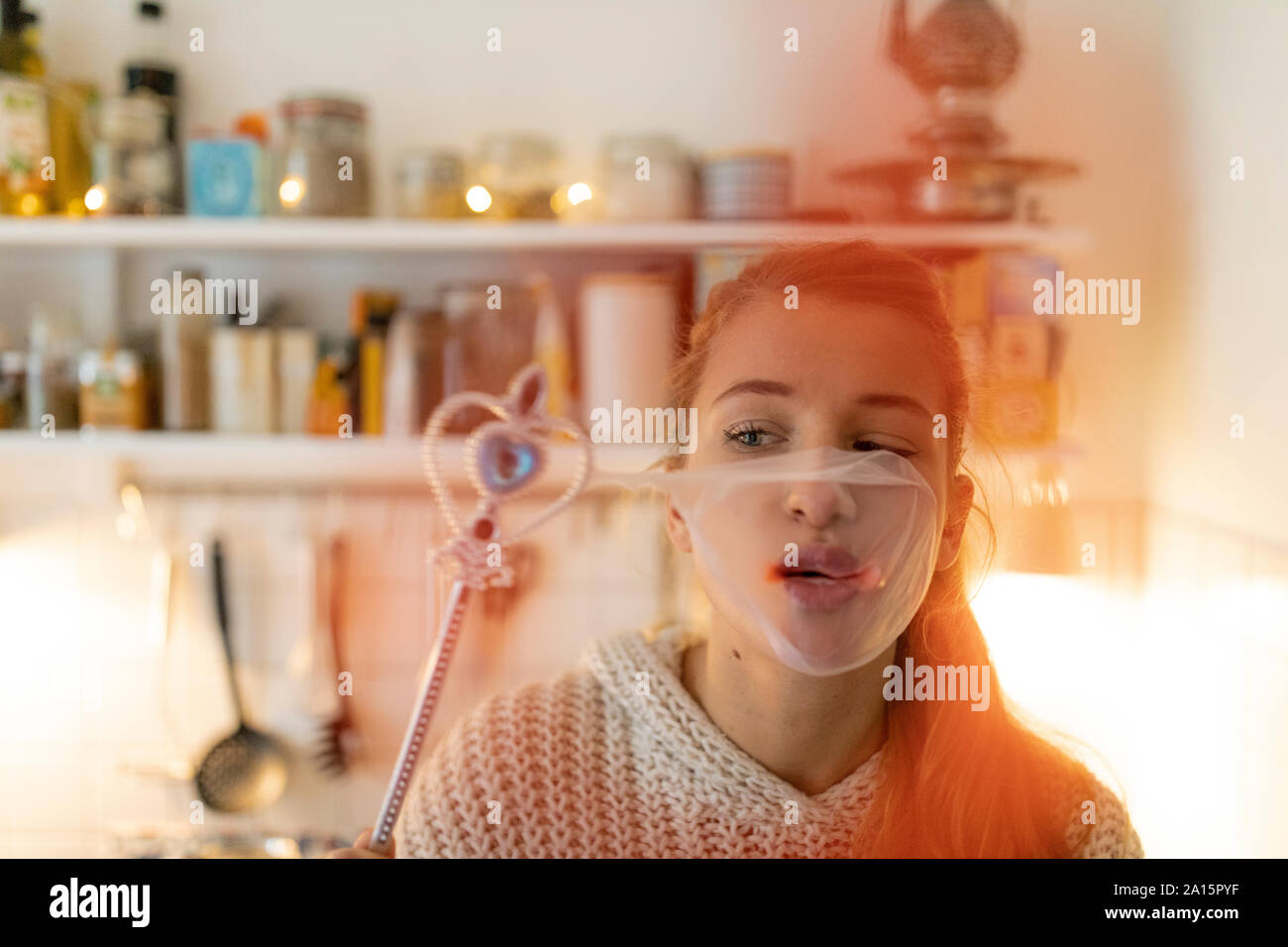 Jeune femme dans la cuisine à la maison avec la baguette magique et de l'éclatement de la bulle de chewing-gum Banque D'Images