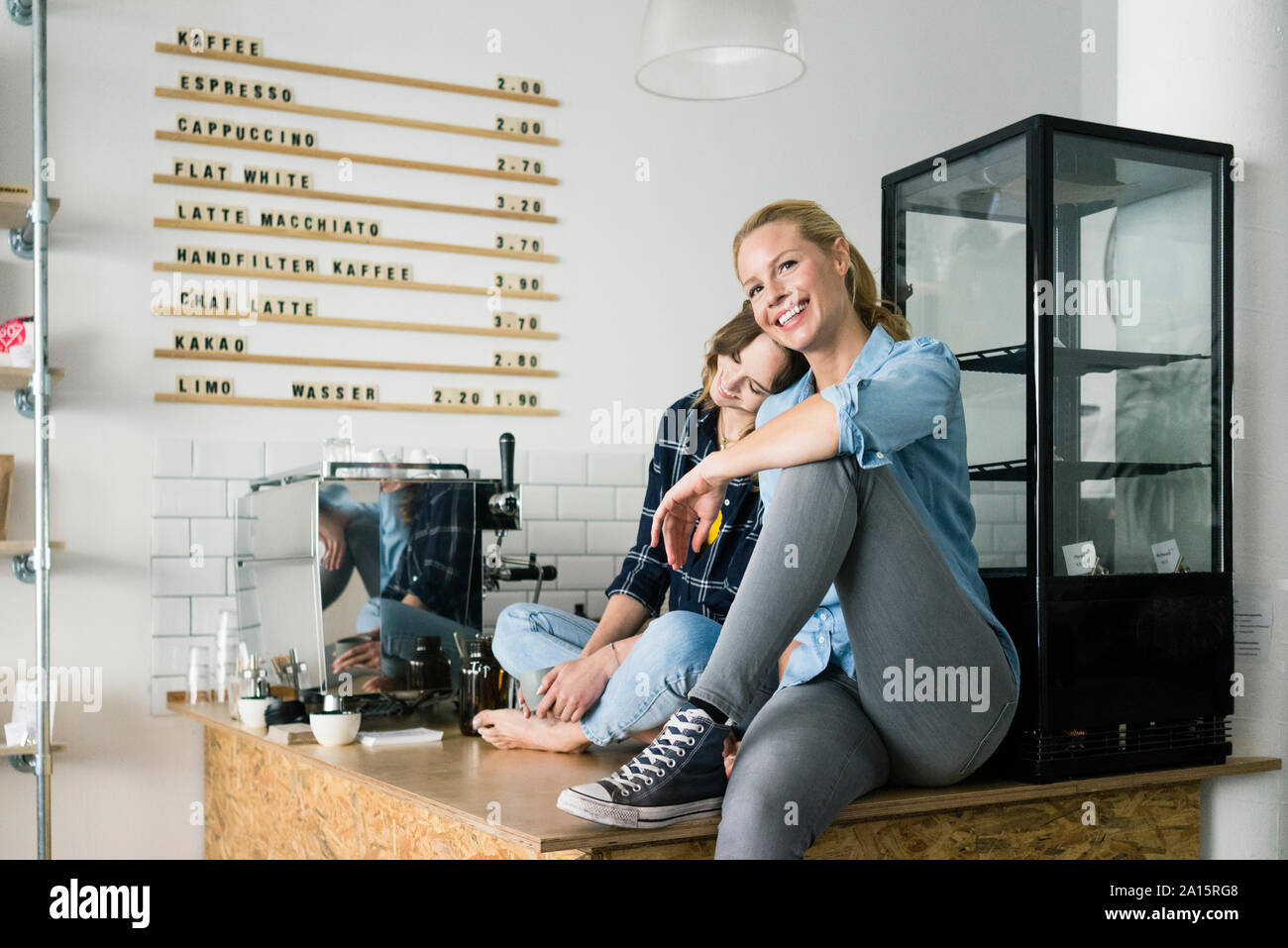 Deux jeunes femmes assises sur le comptoir de leur coffee shop Banque D'Images