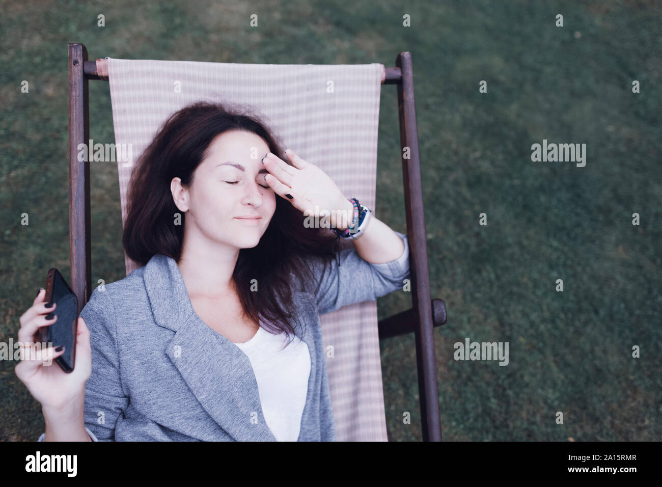 Relaxed woman with cell phone lying dans transat, dans jardin Banque D'Images