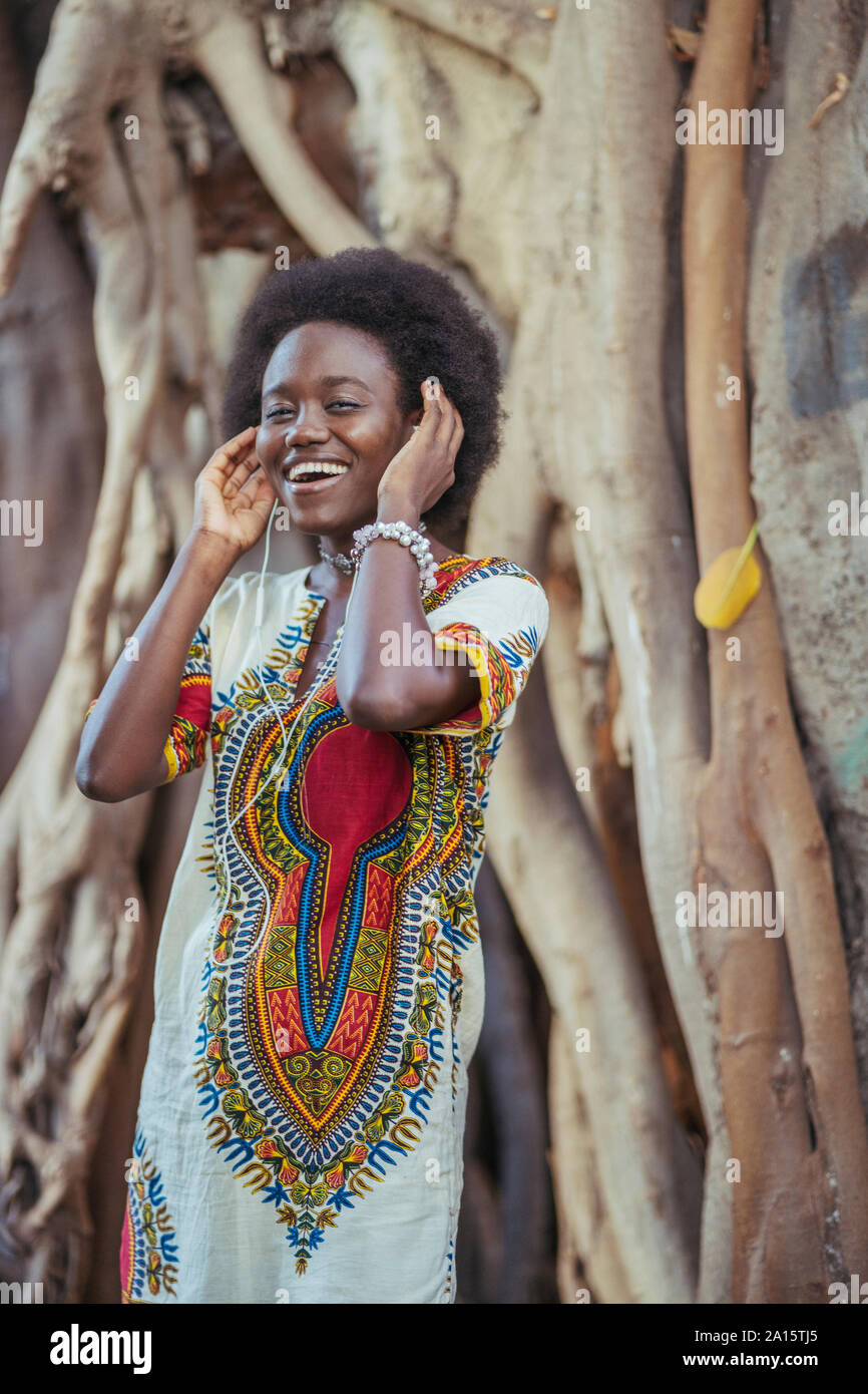 Jeune femme debout devant un tronc d'arbre wearing earphones Banque D'Images
