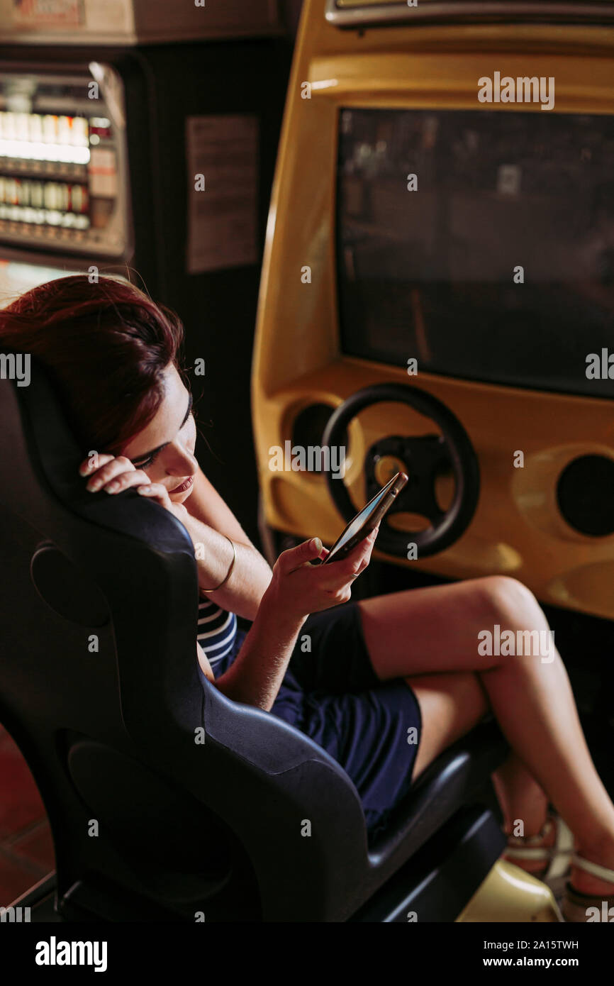 Young woman using cell phone dans un simulateur de conduite dans un bar sportif Banque D'Images