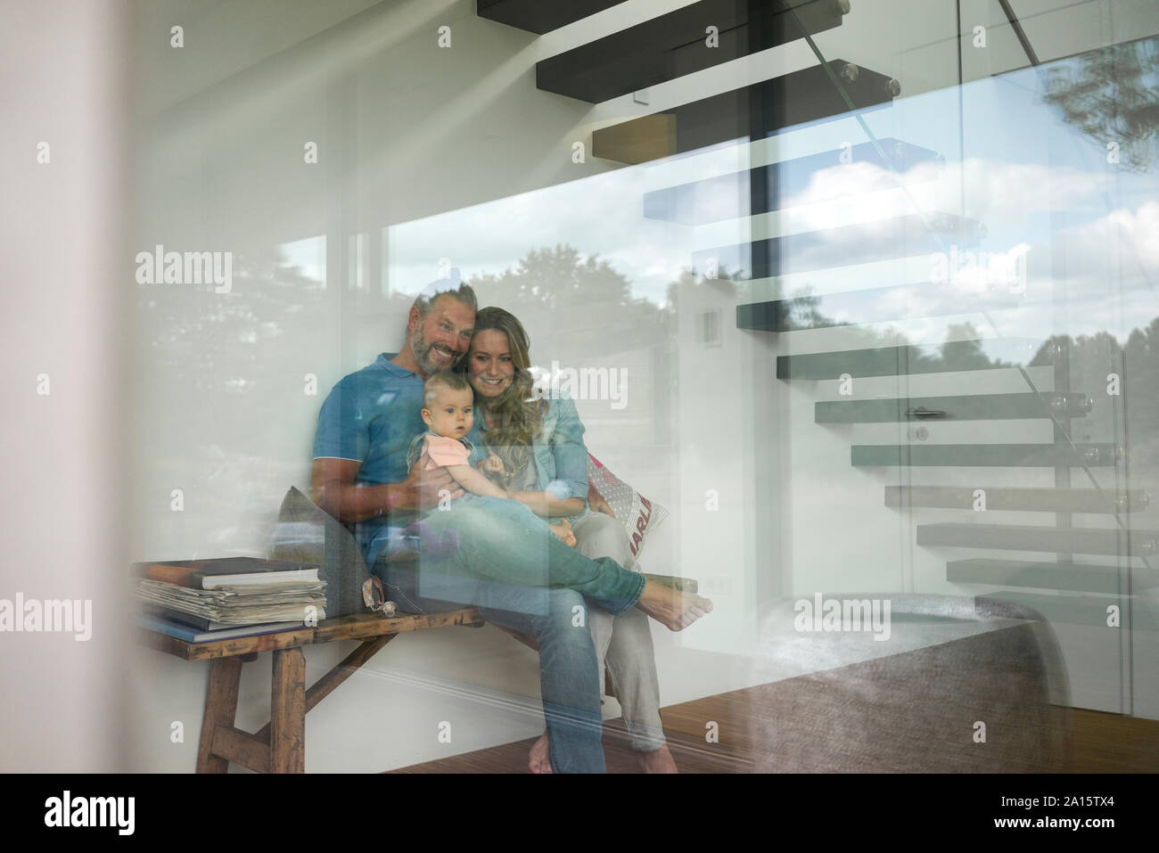 Une famille heureuse de trois assis sur un banc derrière la vitre à la maison Banque D'Images