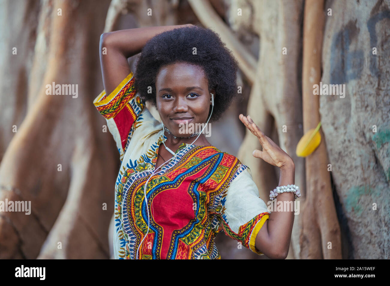 Jeune femme debout devant un tronc d'arbre wearing earphones Banque D'Images