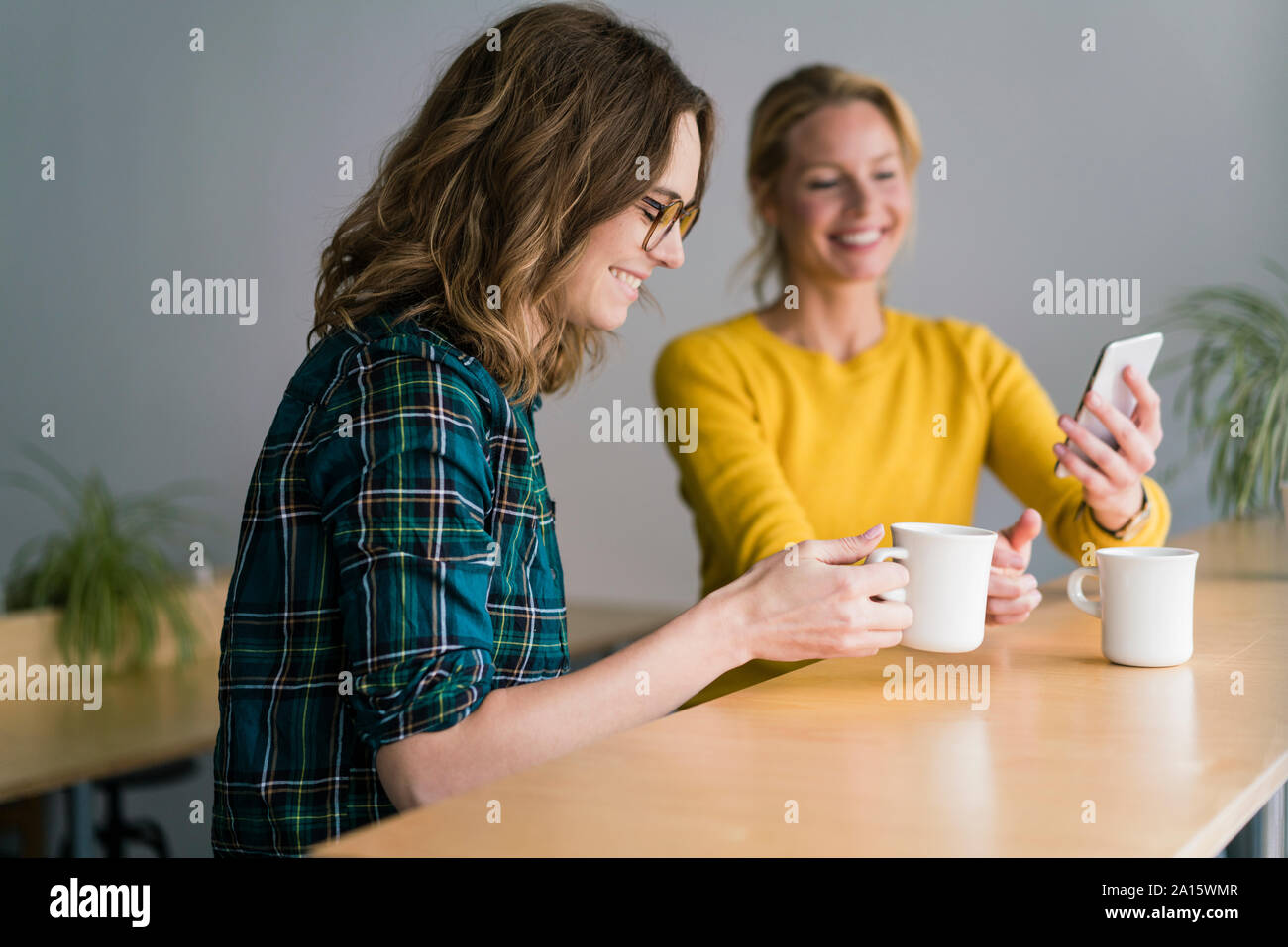 Deux copines assis dans un café, boire du café, using smartphone Banque D'Images
