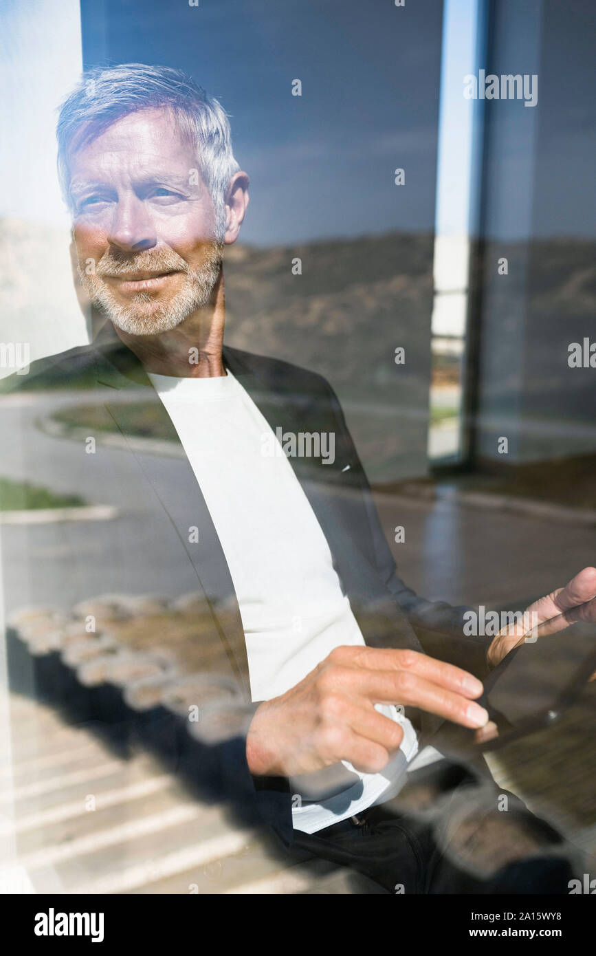Smiling senior businessman using tablet à la fenêtre Banque D'Images