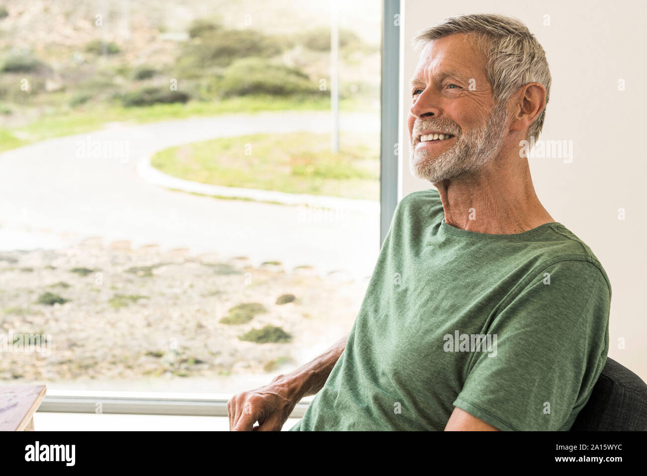 Smiling senior homme assis à la fenêtre à la maison Banque D'Images