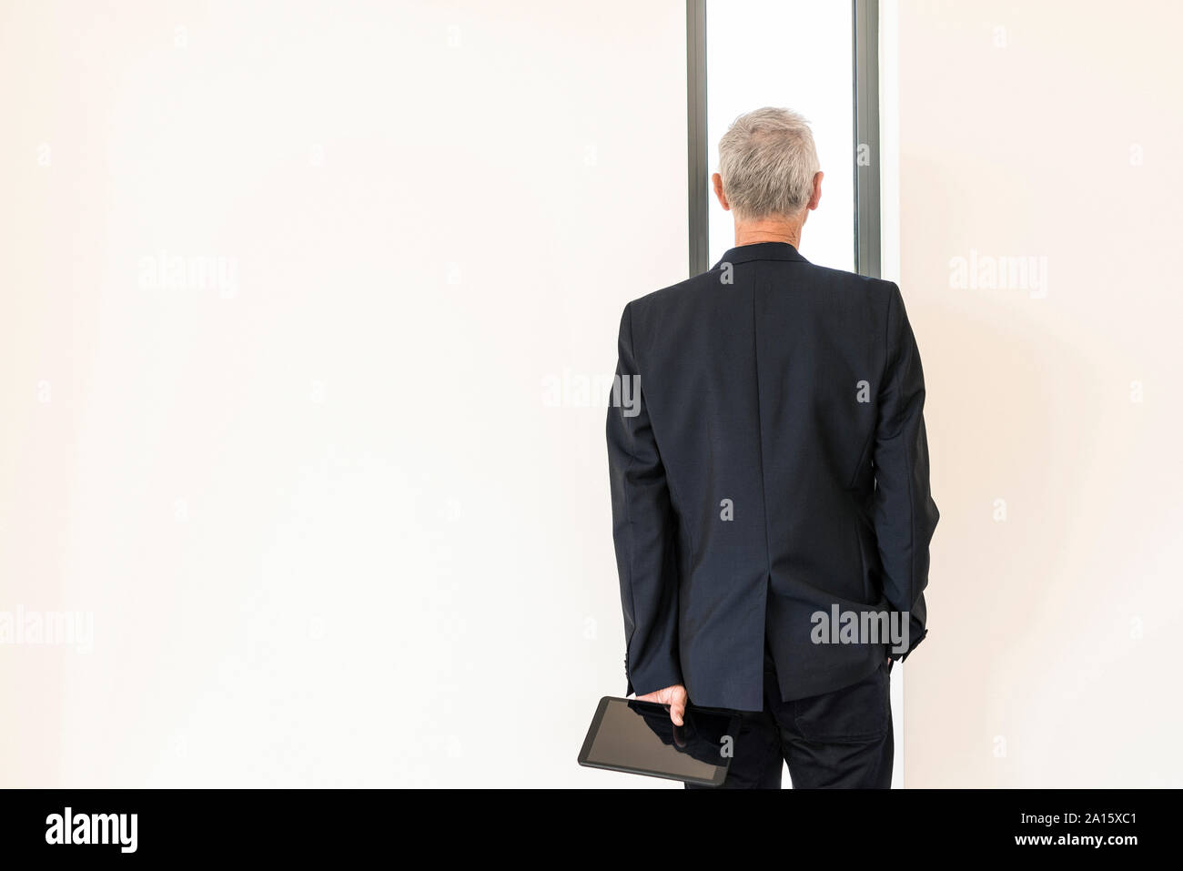 Vue arrière du senior businessman with tablet à la recherche d'une fenêtre Banque D'Images