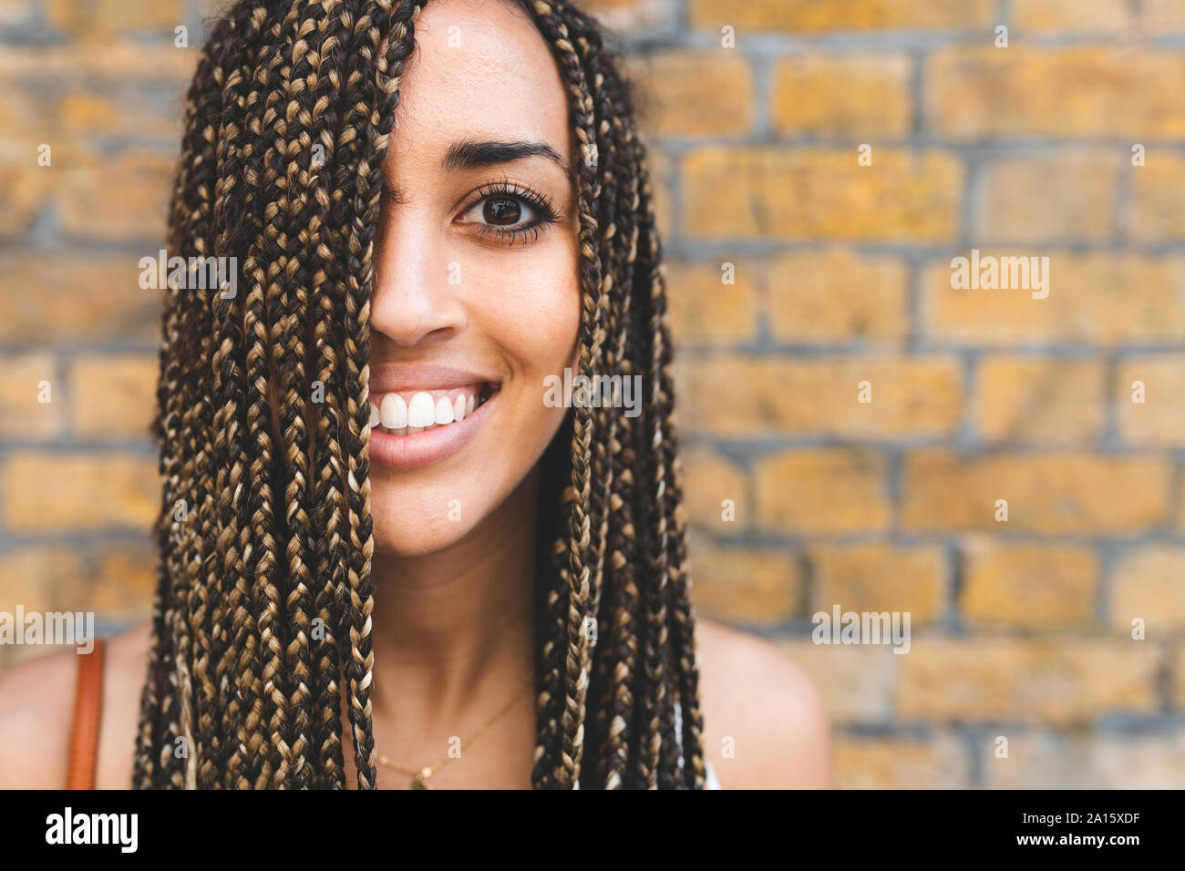 Portrait de jeune femme heureuse avec de longues tresses en avant du mur de brique Banque D'Images