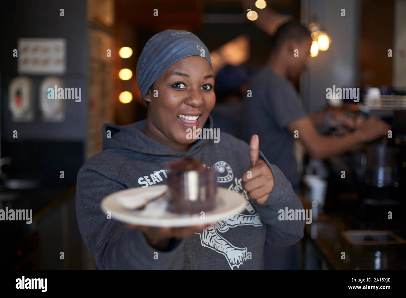 Jeune femme travaillant au café montrant un gâteau Banque D'Images