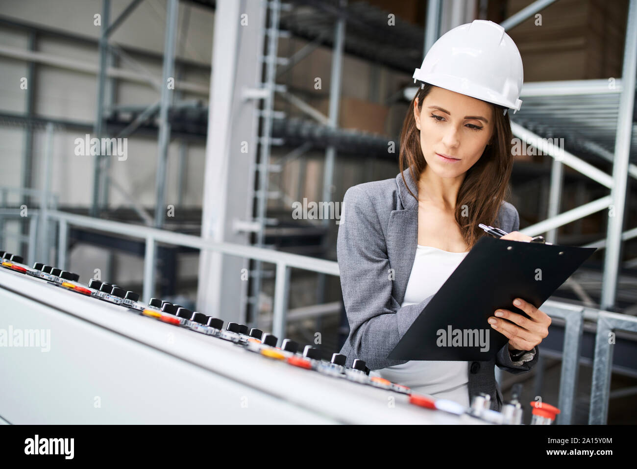 Woman wearing hard hat sur le panneau dans une usine à prendre des notes Banque D'Images