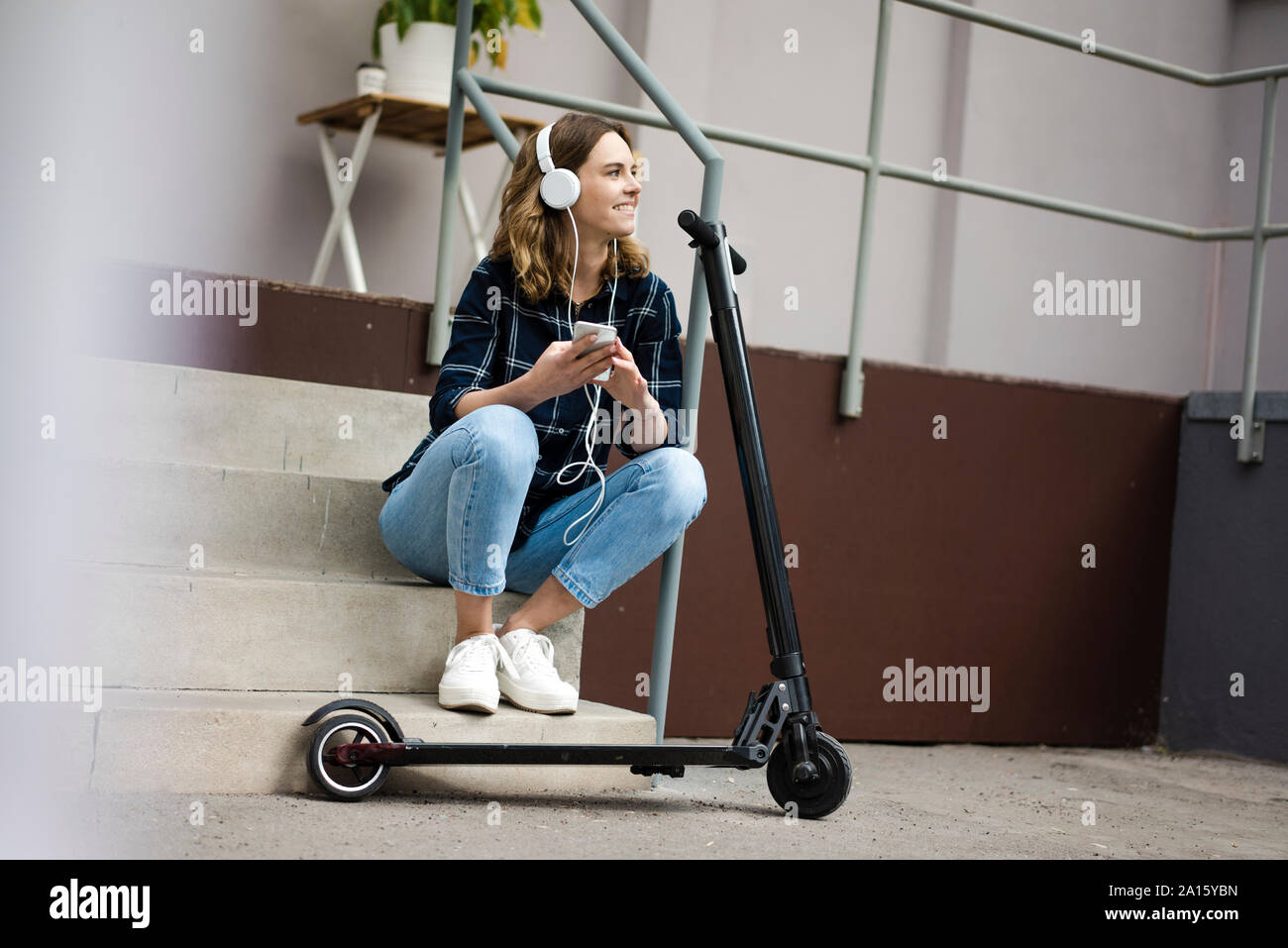 Les jeunes womanwith scooter électrique, assis sur les escaliers, écoutant de la musique Banque D'Images