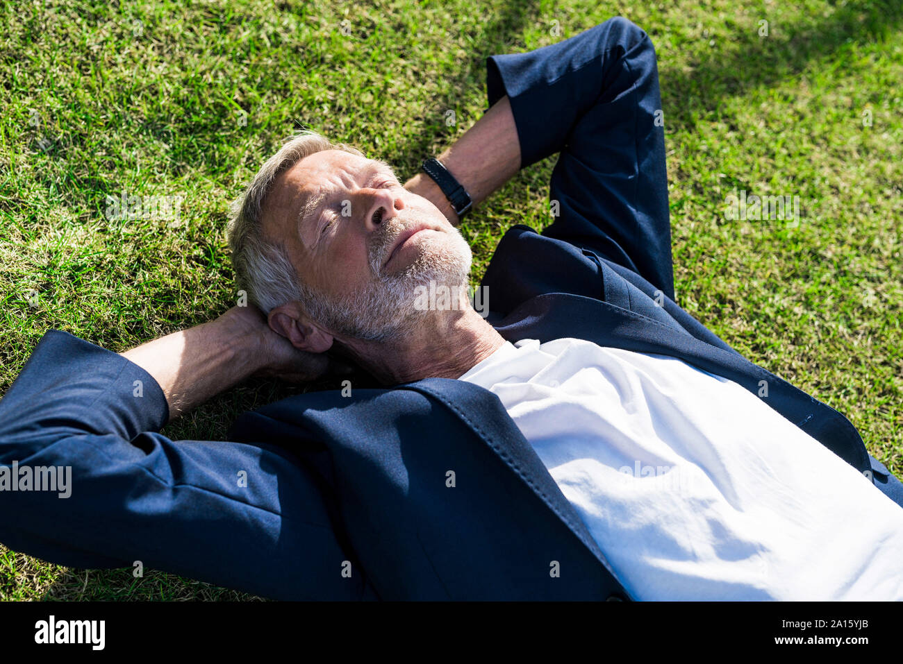 Senior businessman lying in grass with closed eyes Banque D'Images