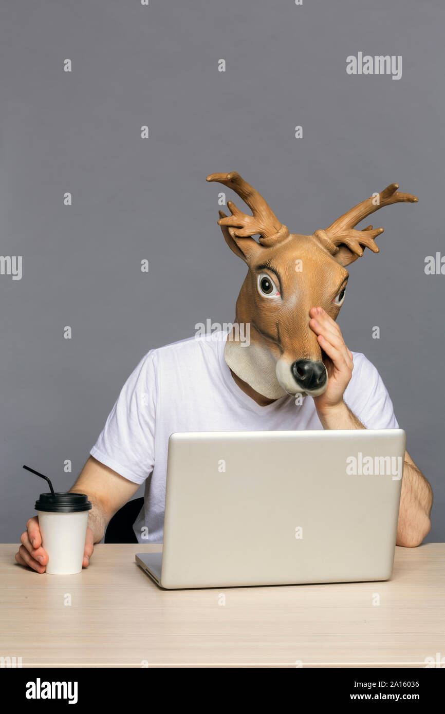 L'homme avec masque à l'aide de cerfs, ordinateur portable pour aller boire du café tasse Banque D'Images