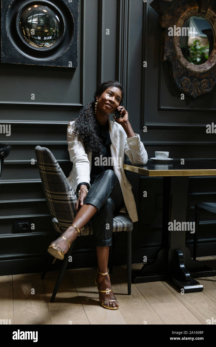 Femme chic sur téléphone cellulaire assis à table dans un café Banque D'Images