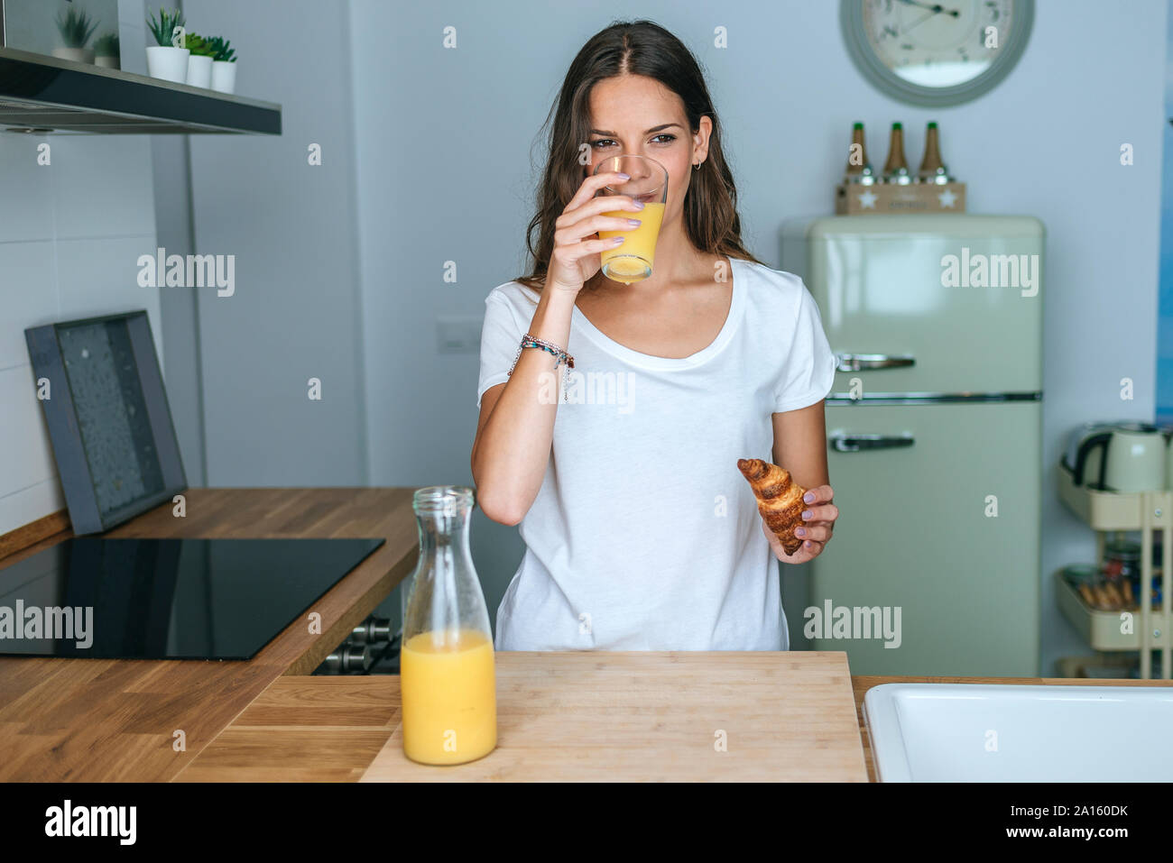 Jeune femme ayant le petit déjeuner avec du jus de fruit et un croissant dans la cuisine Banque D'Images
