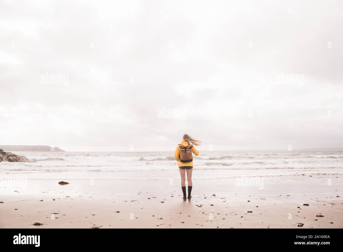 Vue arrière du woman Veste pluie jaune debout à beach Banque D'Images