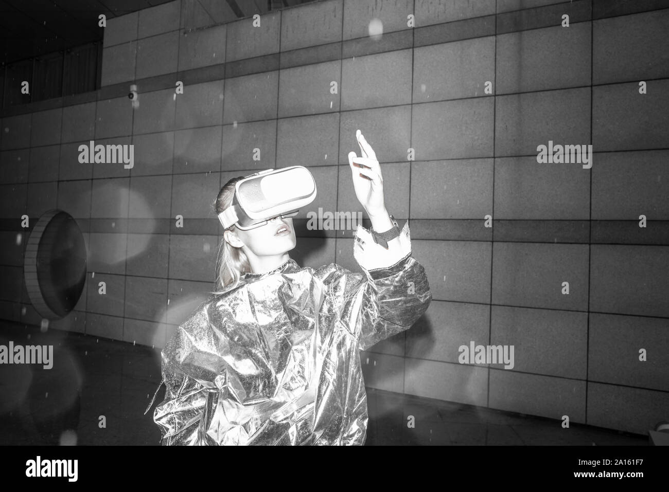 Fille en costume d'argent à la recherche à travers les lunettes de VR, regardant sa main Banque D'Images