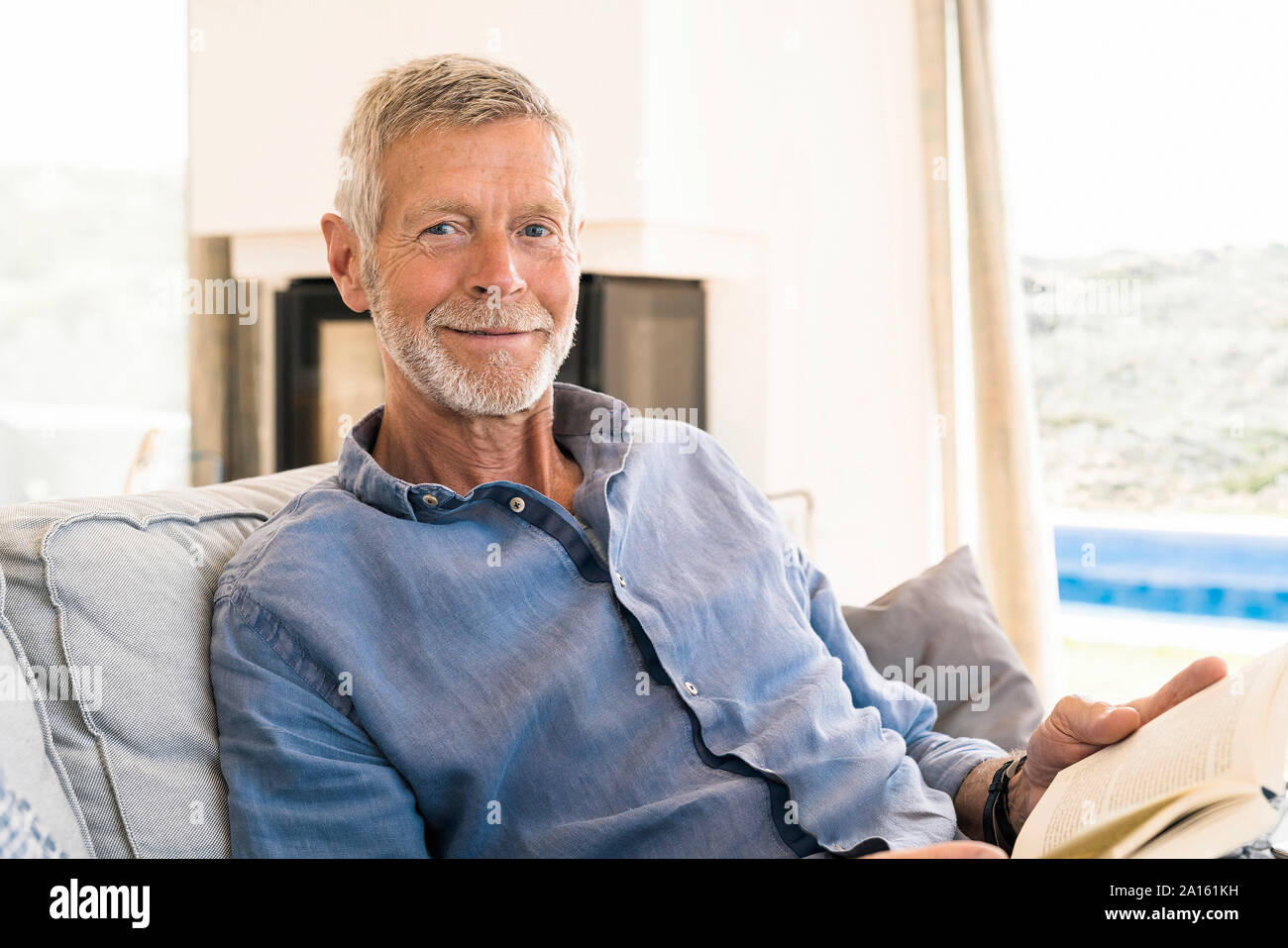 Portrait of smiling senior man reading a book at home Banque D'Images