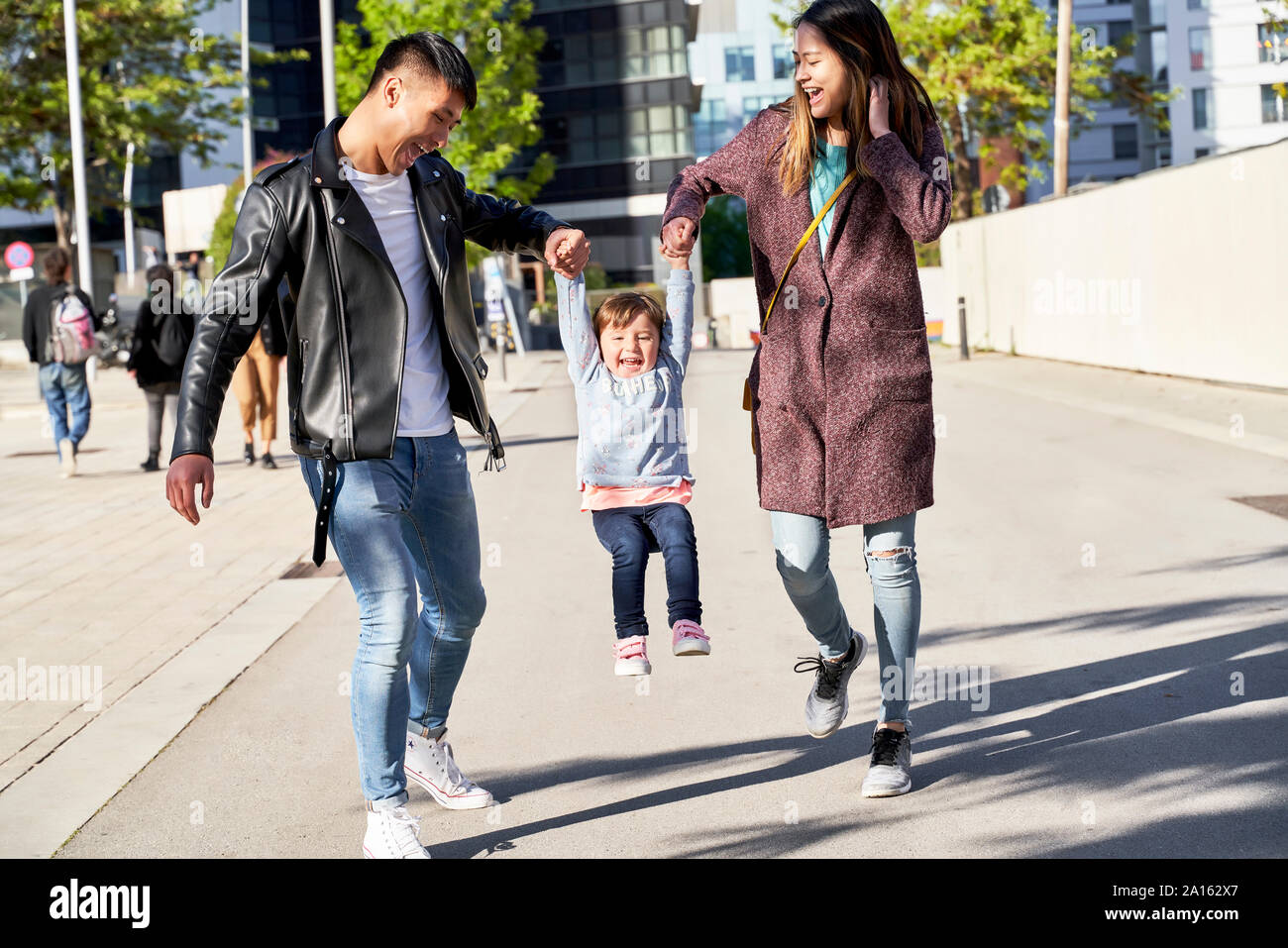 Heureux parents tenant la main de petite fille lors d'un saut, Barcelone, Espagne Banque D'Images