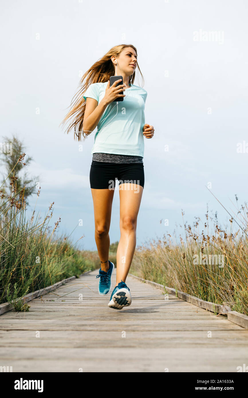 Female jogger running on allée en bois, écouter de la musique Banque D'Images