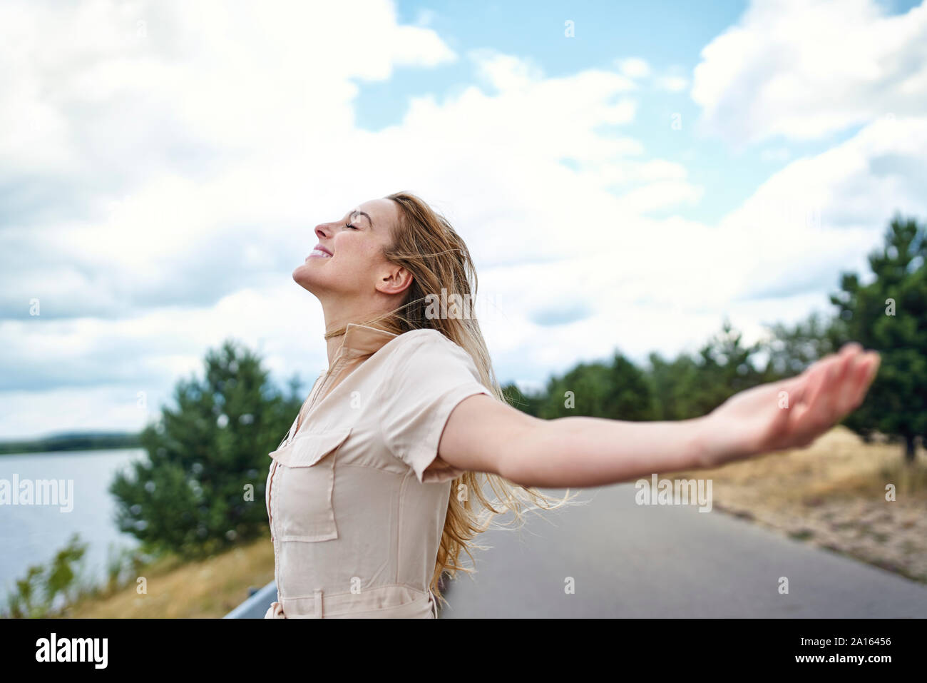 Heureux femme debout au bord de lac avec les bras tendus Banque D'Images Heureux femme debout au bord de lac avec les bras tendus Banque D'Images