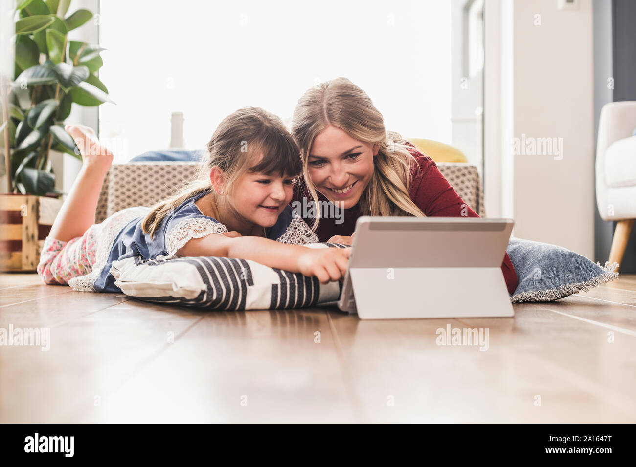 Mère et fille se trouvant sur le plancher à la maison à l'aide de tablet Banque D'Images