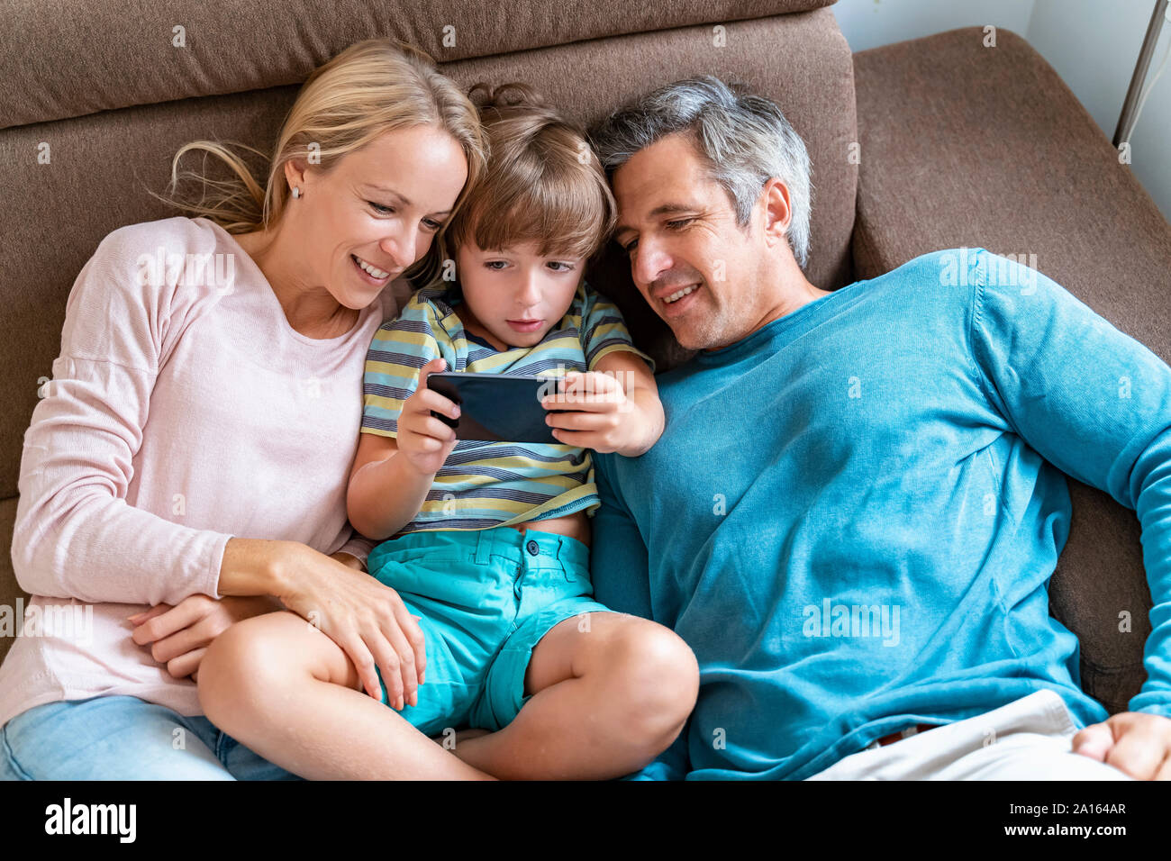 Père, mère et fils using cell phone on sofa at home Banque D'Images