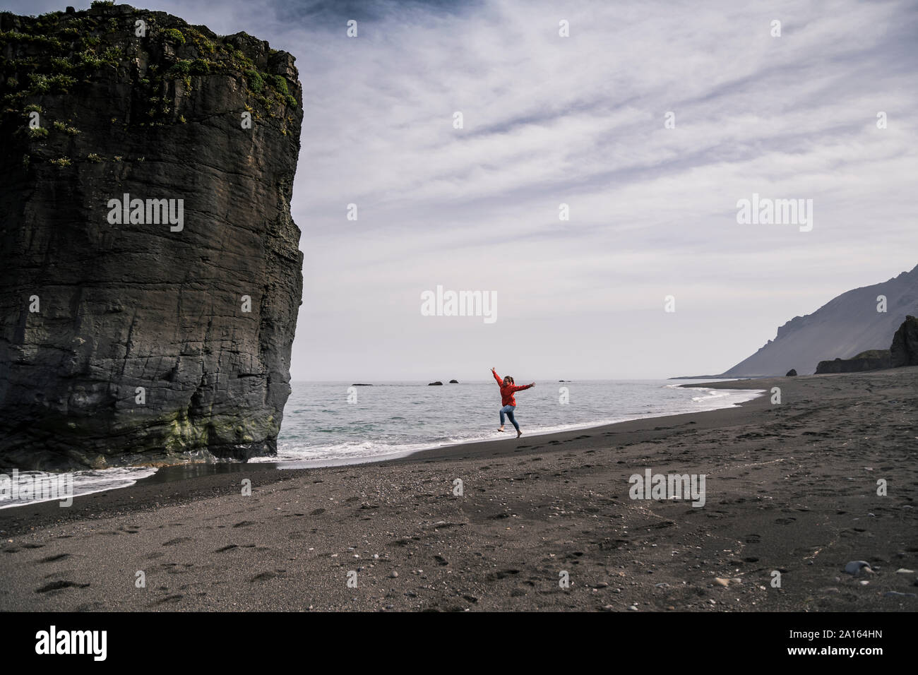 Femme sur une plage dans le sud-est de l'Islande, courir et sauter de joie Banque D'Images