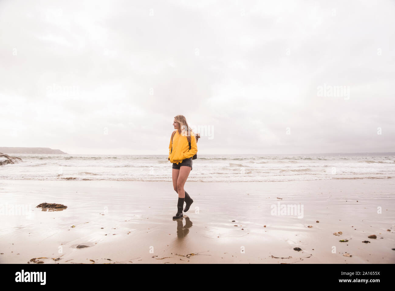 Woman Veste pluie jaune marche à la plage Banque D'Images