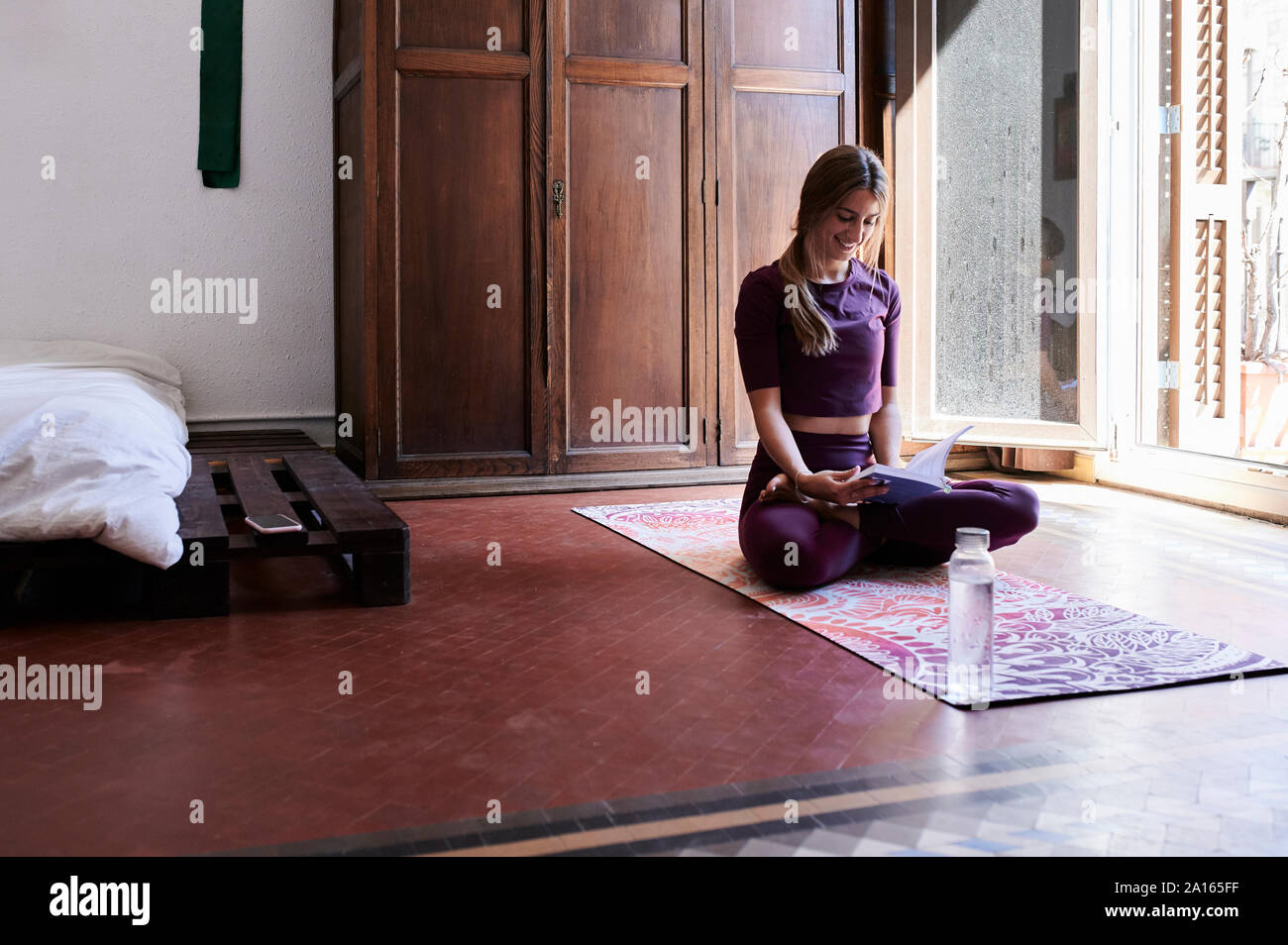 Jeune brunette woman practicing yoga in chambres d'étudiants, la lecture d'un livre Banque D'Images