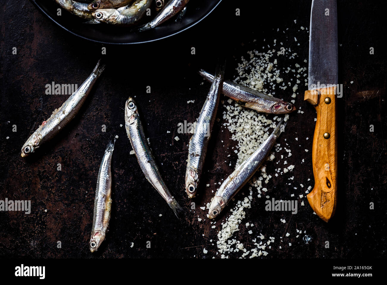 Close-up d'anchois frais et de sel de mer à l'aide d'un couteau sur ardoise noir rock Banque D'Images