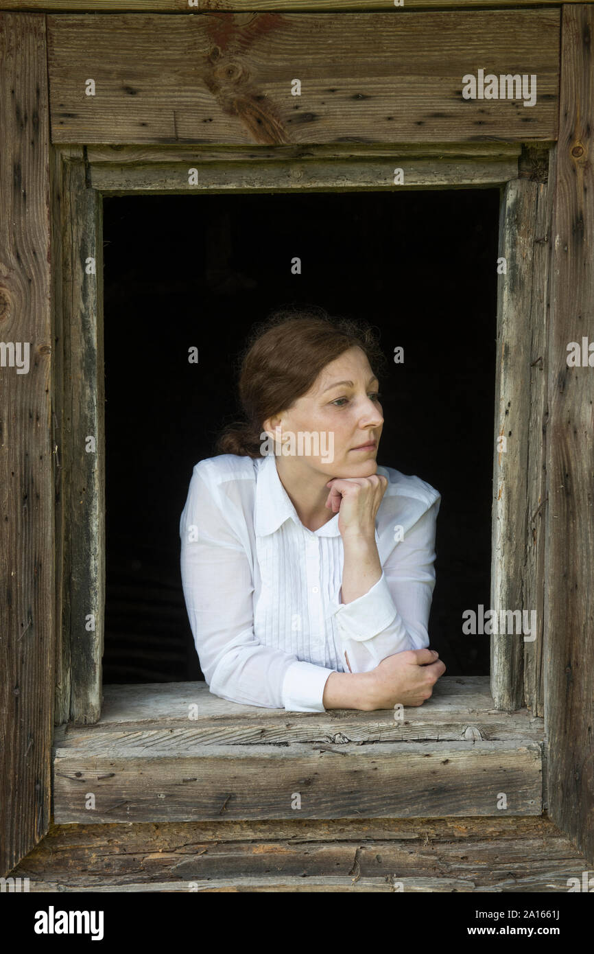Femme à la fenêtre de d'une vieille maison en bois Banque D'Images