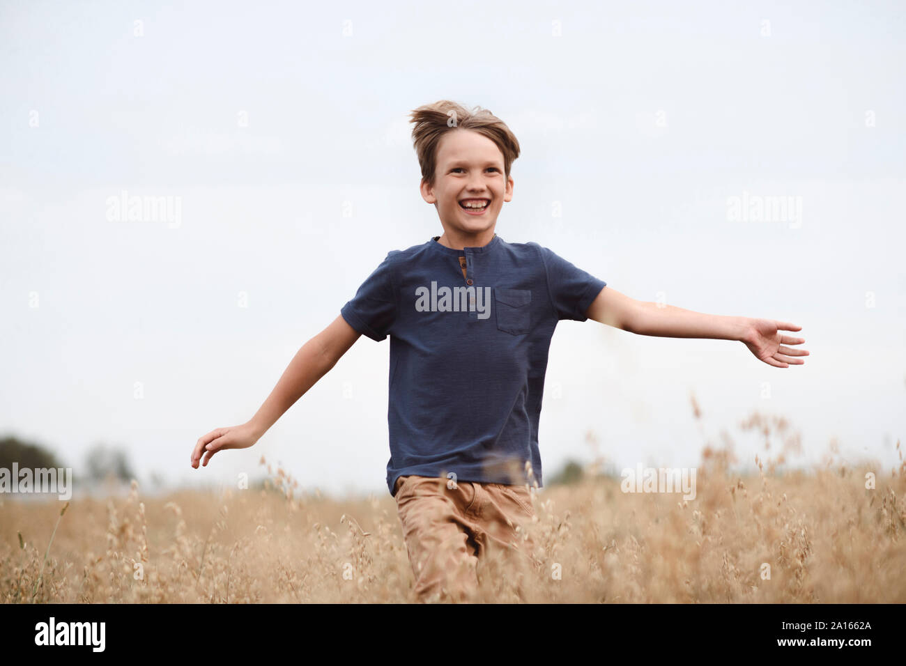Portrait of laughing boy running dans un champ d'avoine Banque D'Images