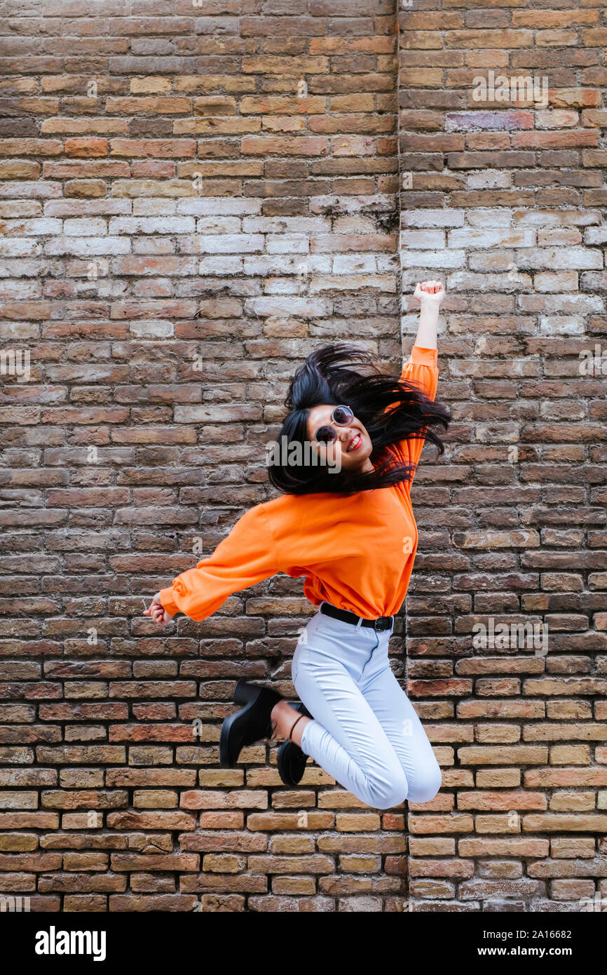 Asian woman jumping, mur de brique à l'arrière-plan Banque D'Images